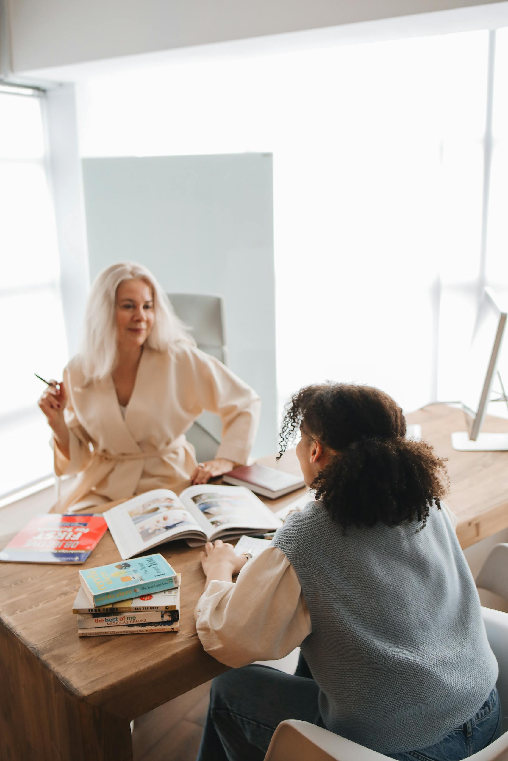 Two women discussing books in a bright room, highlighting education and collaboration.