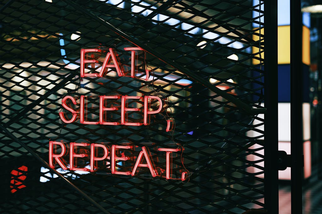 Close-up of a vibrant neon sign with the slogan 'Eat, Sleep, Repeat' on a metal grate background.